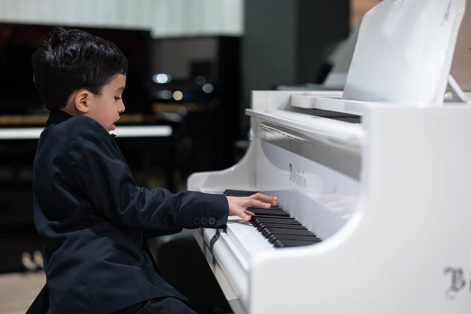 Young boy playing a white grand piano